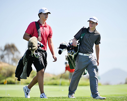 two young golfers walking with their bags on the course during the day