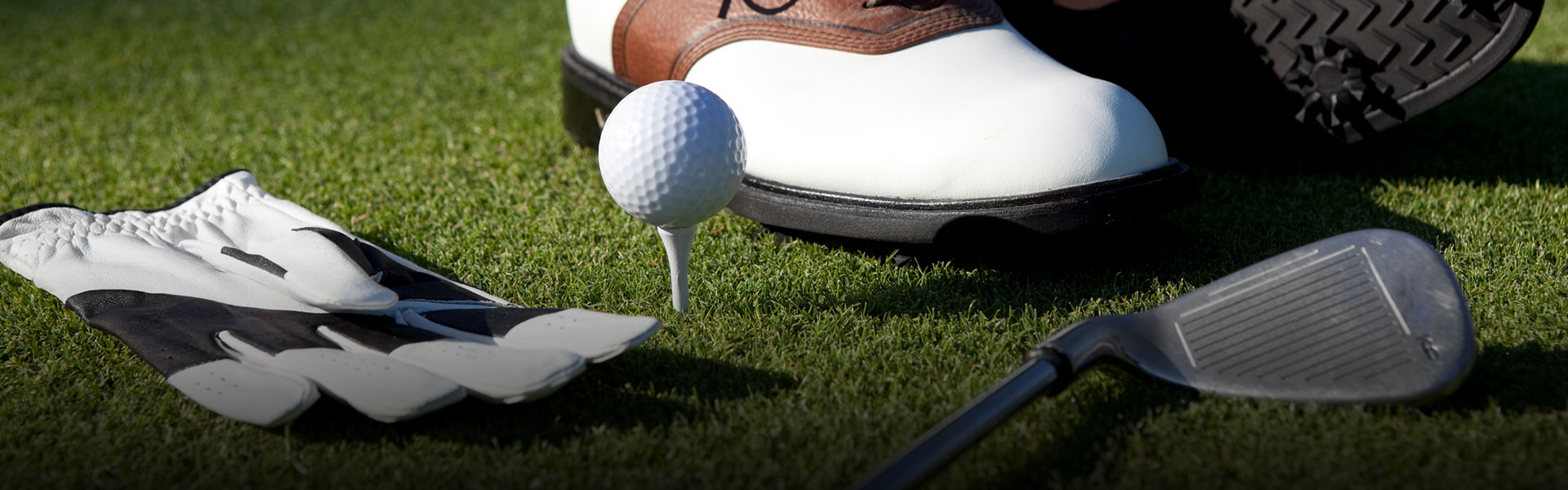 close up of a ball on a tee, golf club, and glove