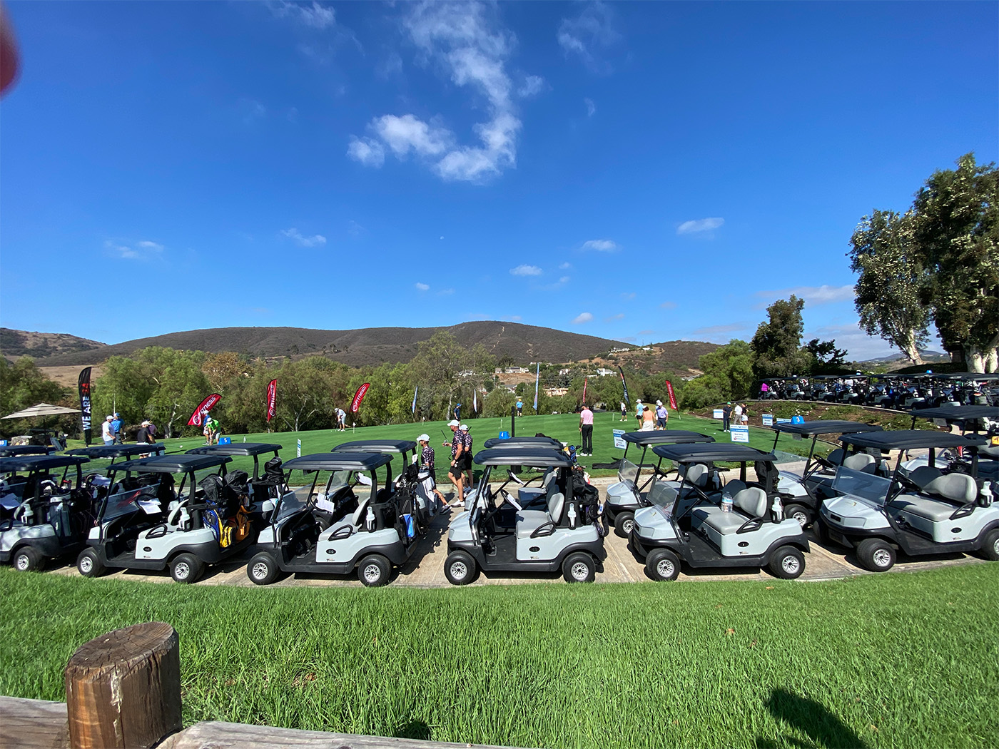 many golf carts parked next to the golf course with golfers nearby