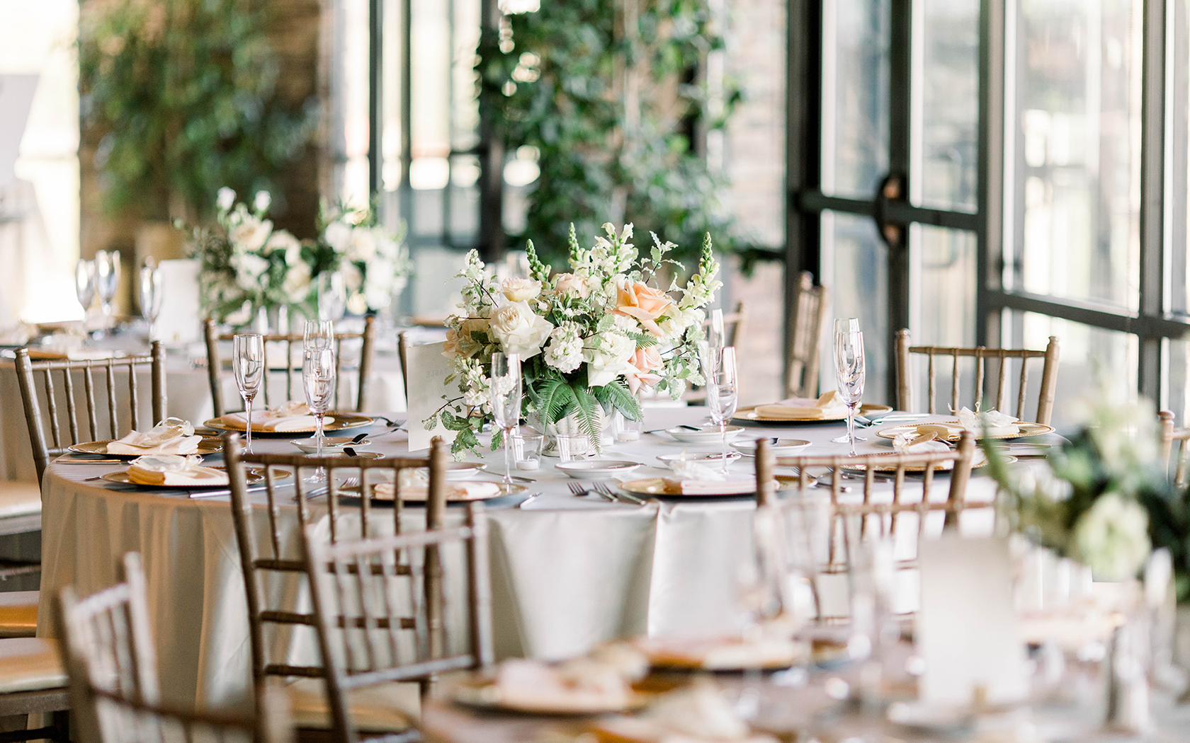 a round linen covered table with a light colored floral centerpiece in the middle