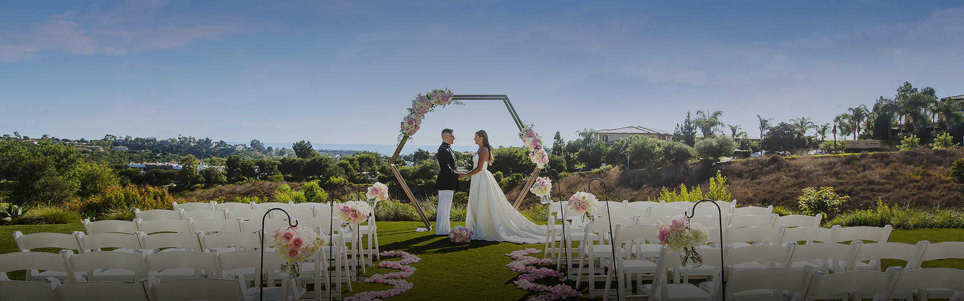 a dim image of a bride and groom standing on the golf course in front of rows of chairs
