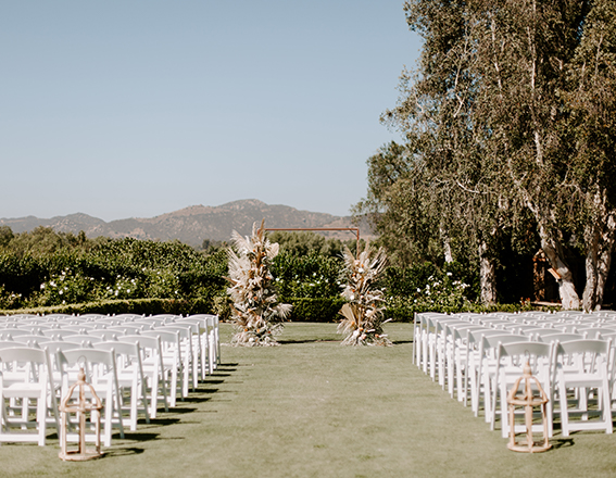 rows of white chairs on the course with a floral arch 