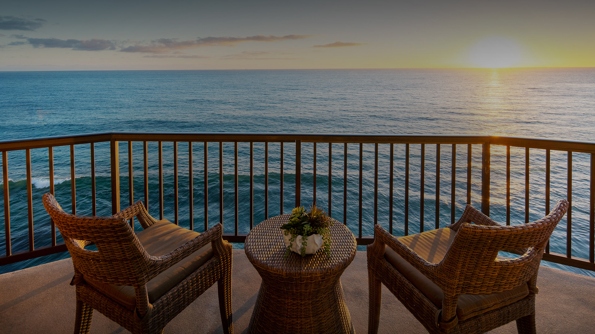 Two wicker chairs on a balcony overlooking the ocean