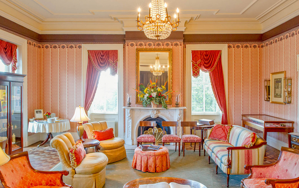 Elegant living space with peach padded chairs, yellow sofa, red curtains & crystal chandelier
