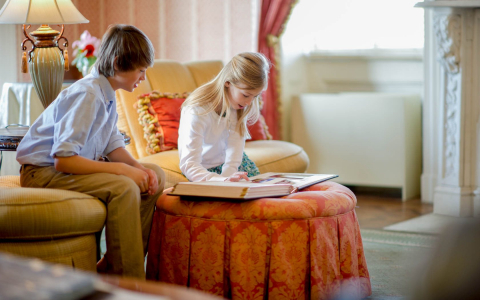 Two kids seated on bright colored furniture looking at photo album