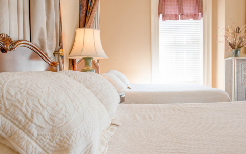 Close up of white pillows on bed with lamp & window in the background