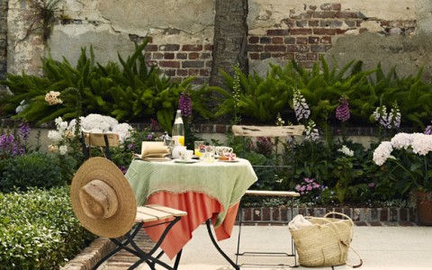 two chairs and a table with bushes in background and bag on floor
