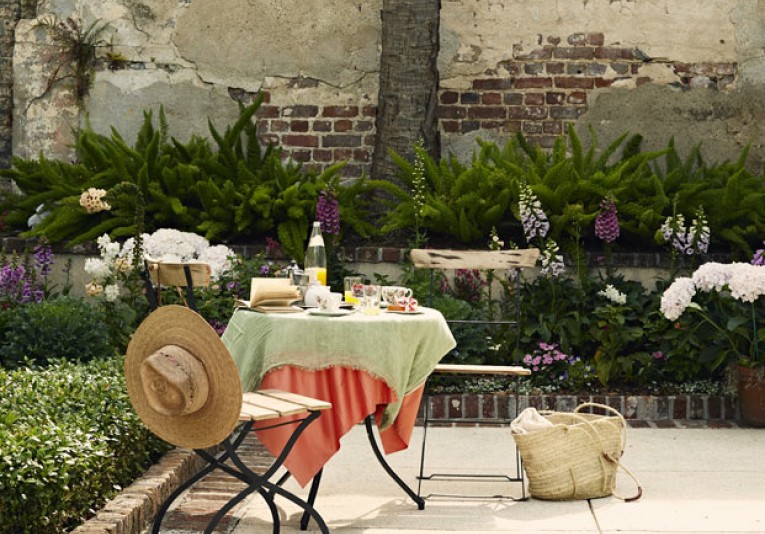 two chairs and a table with bushes in background and bag on floor