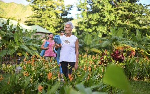 woman walking through a garden with a yoga mat
