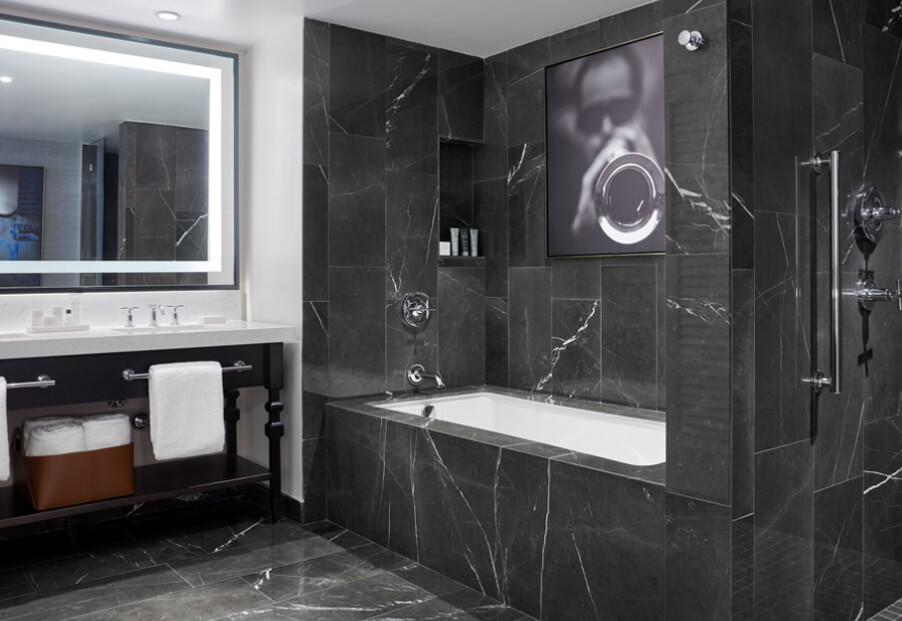 black marble bathroom with tub and lighted mirror