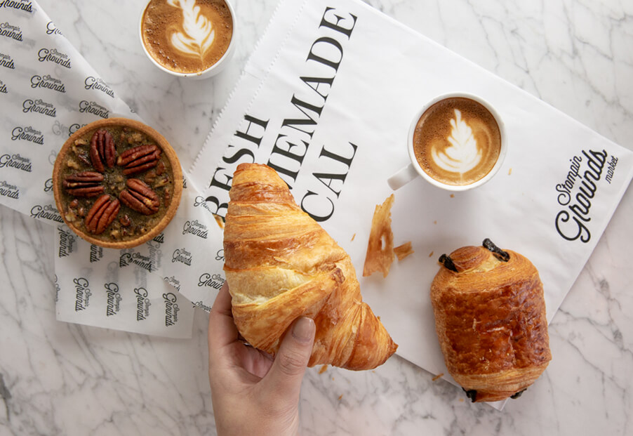 hand holding croissant over table that has coffee and other pastries on it