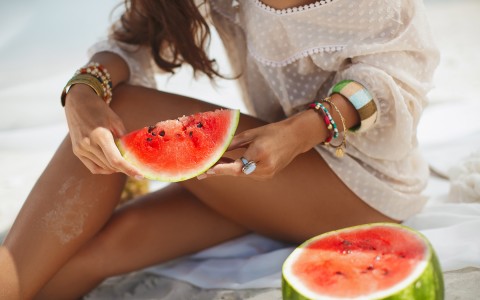 Closeup of a woman holding a slice of watermelon at the beach 