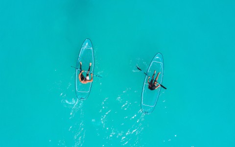 Top view of two people on a cristal explorer kayak on a turquoise sea
