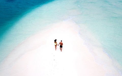 Aerial view of a couple on a pink sand place surrounded by water