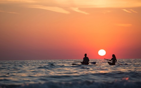 View of the silhouettes of two people surfing on a sunset 