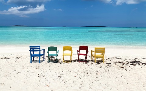 colorful chairs sitting in the sand and facing the water 