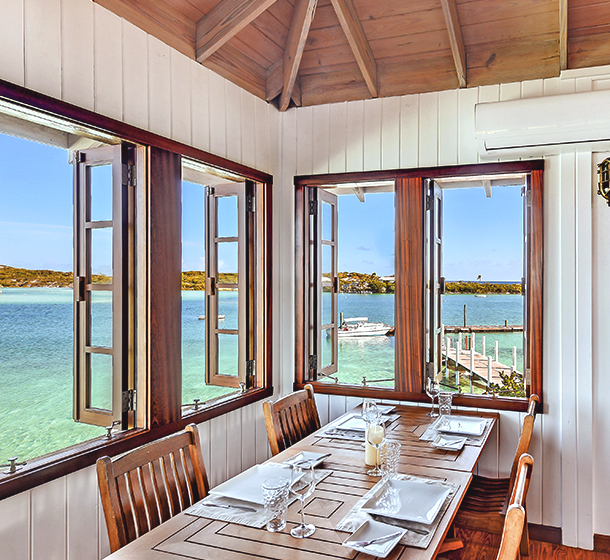 restaurant dining table in the corner of the room next to open windows overlooking the ocean water