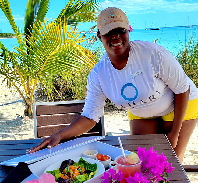 kahari employee smiling while showcasing a food deliver a table on the beach