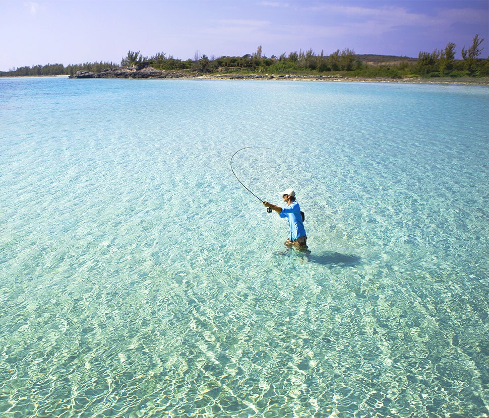 person walking in the water with a fishing rod