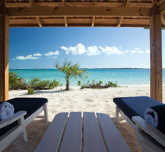 white sand with blue water from under a cabana with two beach chairs