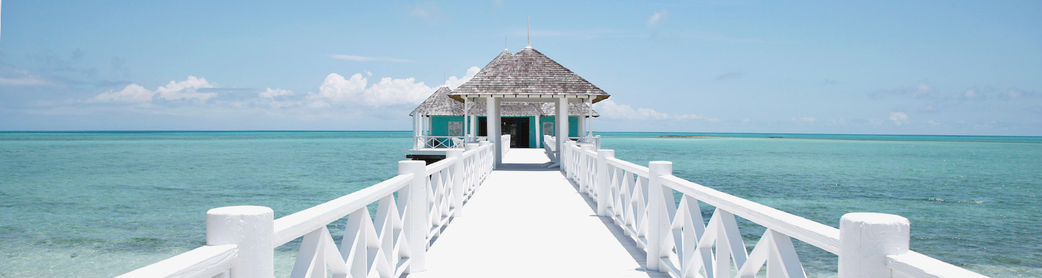 White bridge over bright blue water leading to building