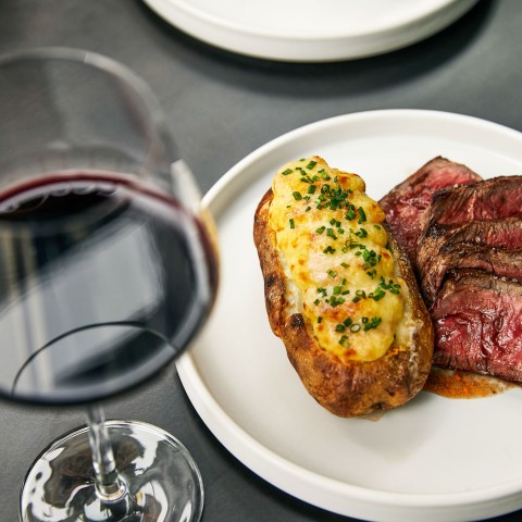plate of steak with a baked potato and red wine glass