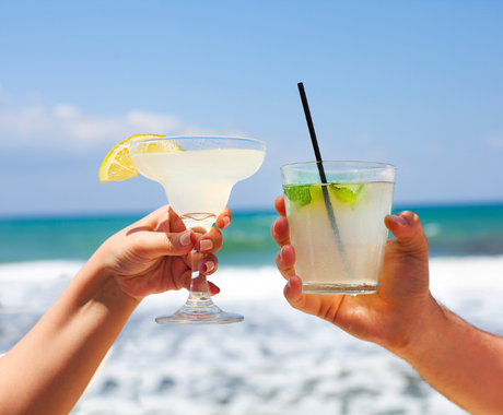 two hands holding different cocktails and cheers posing by beach