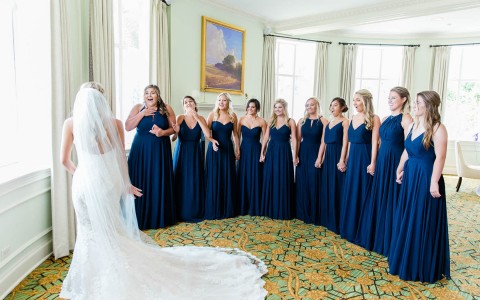 bride standing in front of a semi-circle of her bridesmaids dressed in a dark navy blue