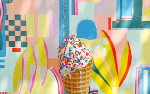 woman holding a icecream cone with sprinkles outside against an abstract art covered wall