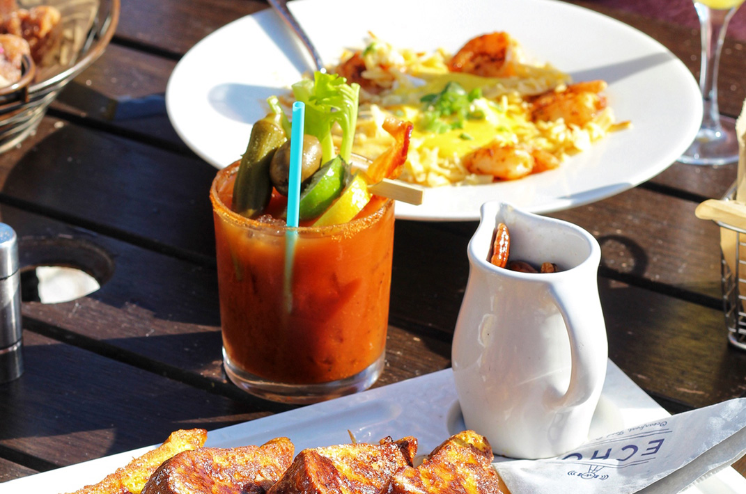 plated breakfast meal of frenchtoast, bloody mary, shrimp and grits on outdoor table