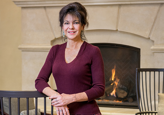 Headshot of Sproattrina - arms resting over chair in front of fireplace