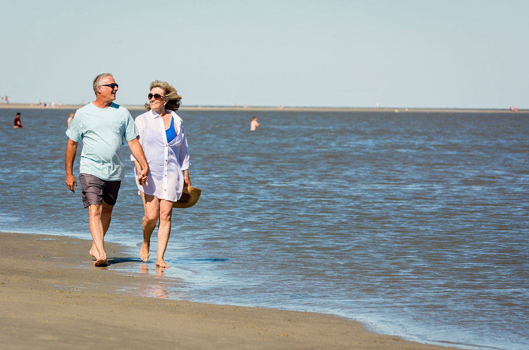older man and woman walking along beach at water's edge
