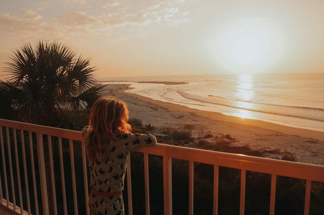 little girls resting on patio fence watching sunrise over calm ocean