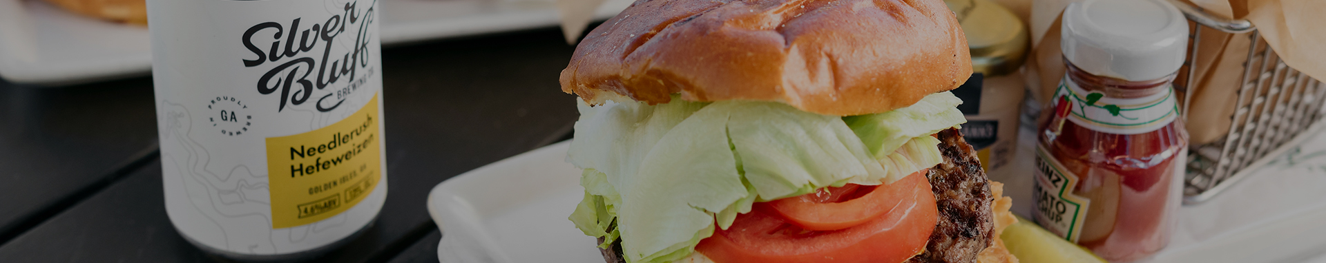 burger meal with fresh lettuce and tomato with can of beer and mini ketchup bottle