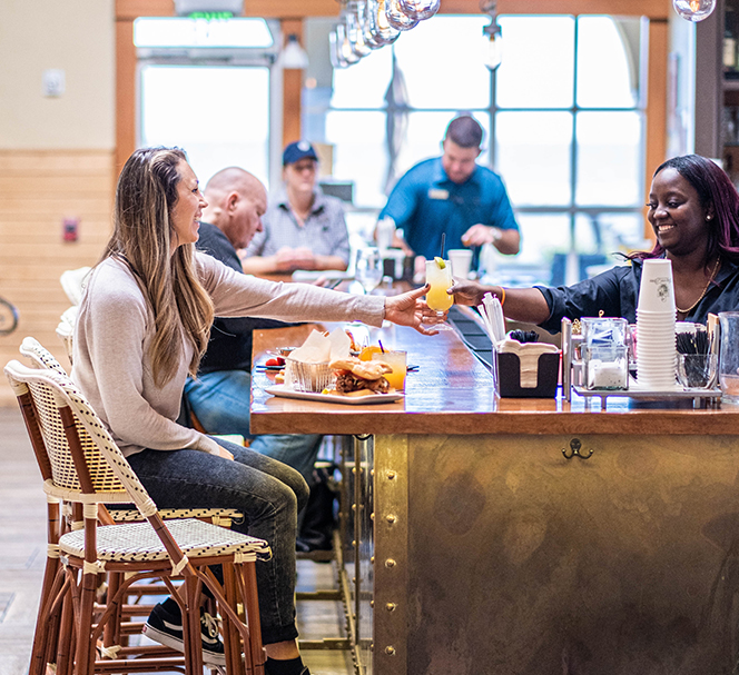 woman enjoying a meal and a drink at the bar of echo getting served by happy bartender