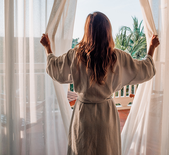 woman in robe opening curtains to look out on large balcony