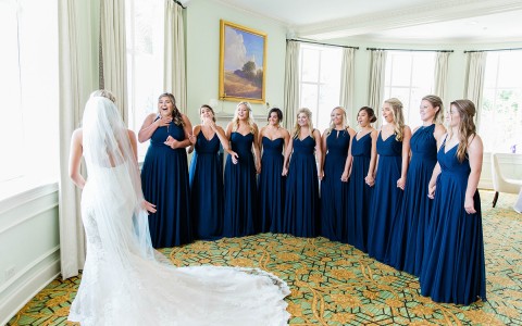 bridesmaids in navy dresses reacting to seeing the bride for the first time