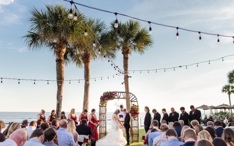 view of a bride and groom at the altar holding hands in front of all of their guests