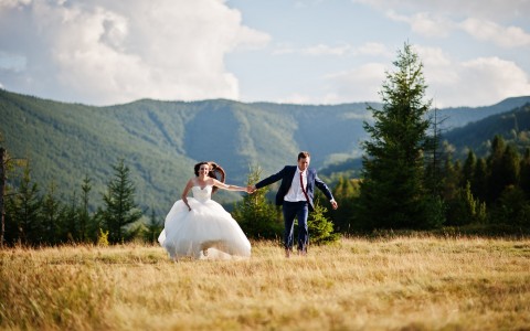 bride and groom holding their hands while they are running in the nature