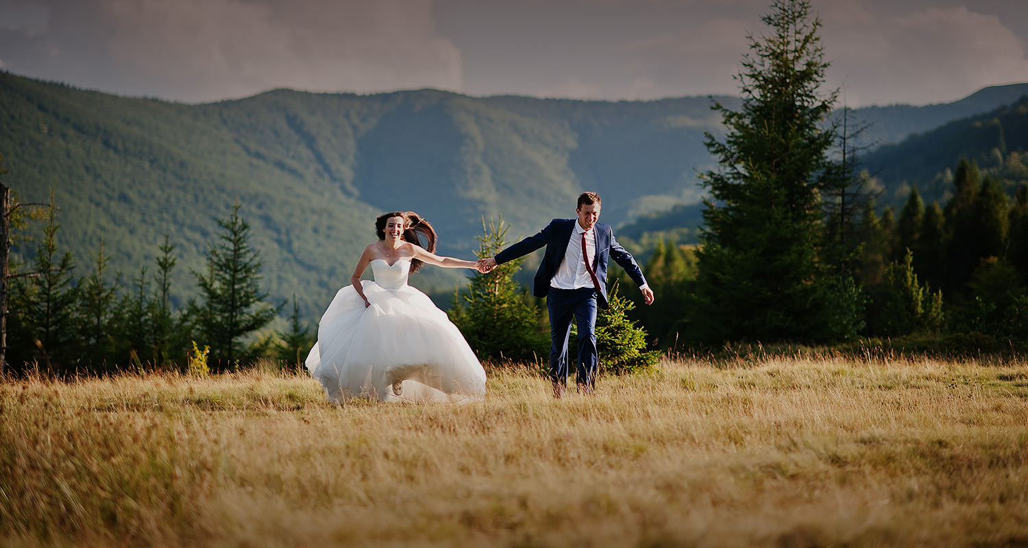 bride and groom running in a field with green mountains in the background 