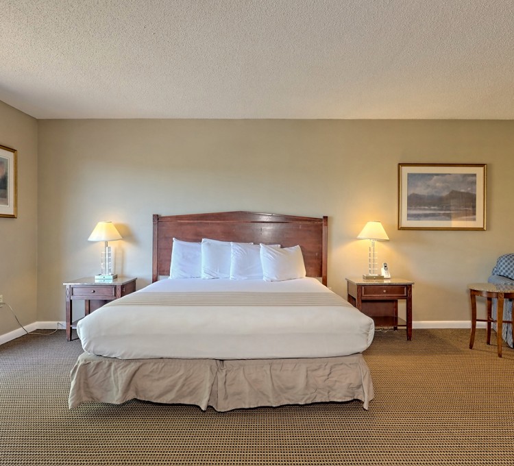 Traditional and spacious hotel room with features as queen bed sized, two nightstands and armchair