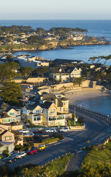 An aerial view of homes and a road near the ocean with the sun setting.