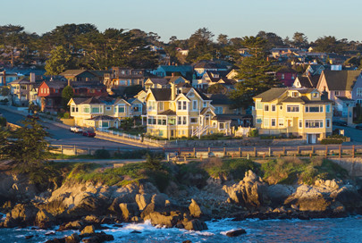 Many houses near the road and coast with the sun setting to the left.