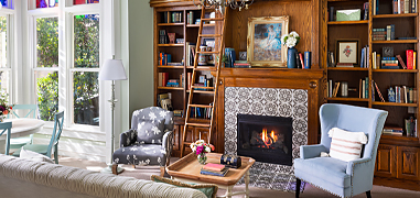 A library with a lit fireplace and seating during the day.