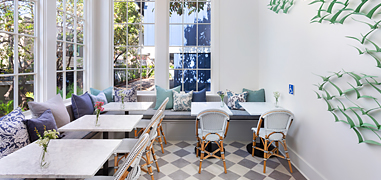 A dining area with white tables and wood chairs during the day.