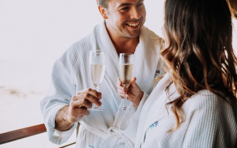 a couple in robes standing on the balcony having champagne