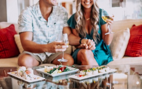 a couple holding hands on the couch while having wine and sushi
