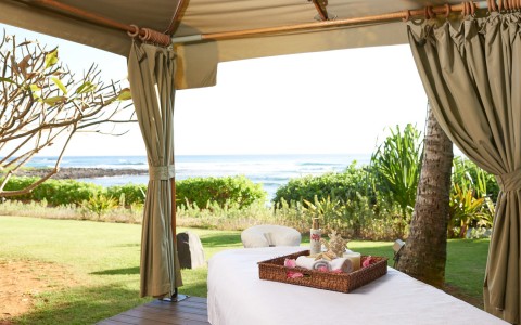 a spa bed with a basket of spa products in a cabana viewing the ocean