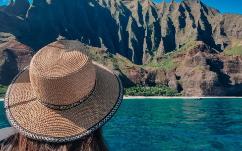 woman with a hat on looking at the mountains from a boat