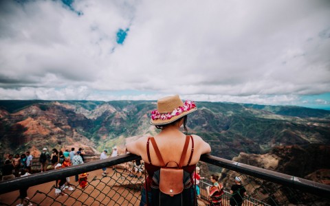 view of a woman with a hat and a lei on looking at the mountains from an overlook